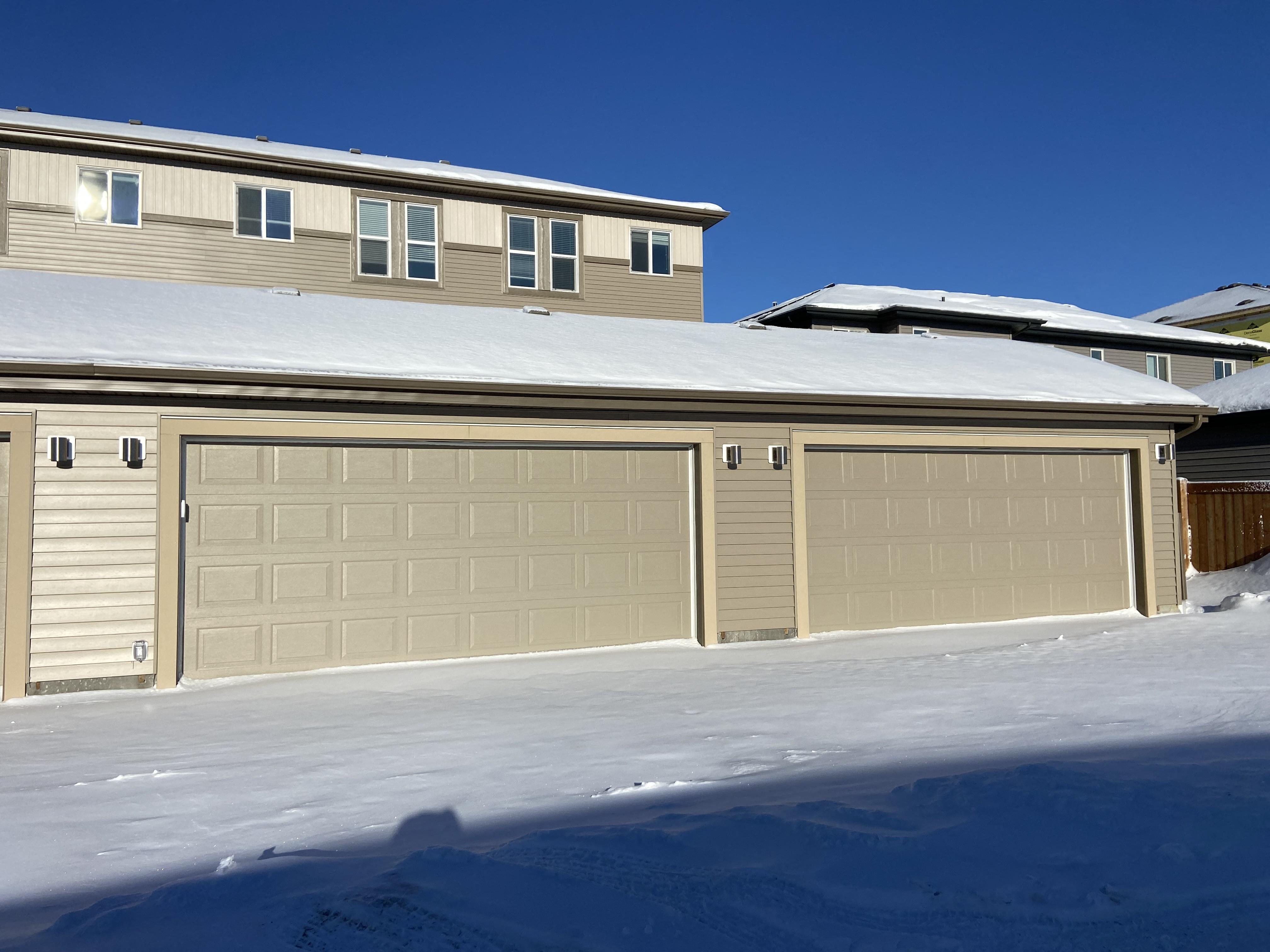 A row of garage doors in front of a house covered in snow.